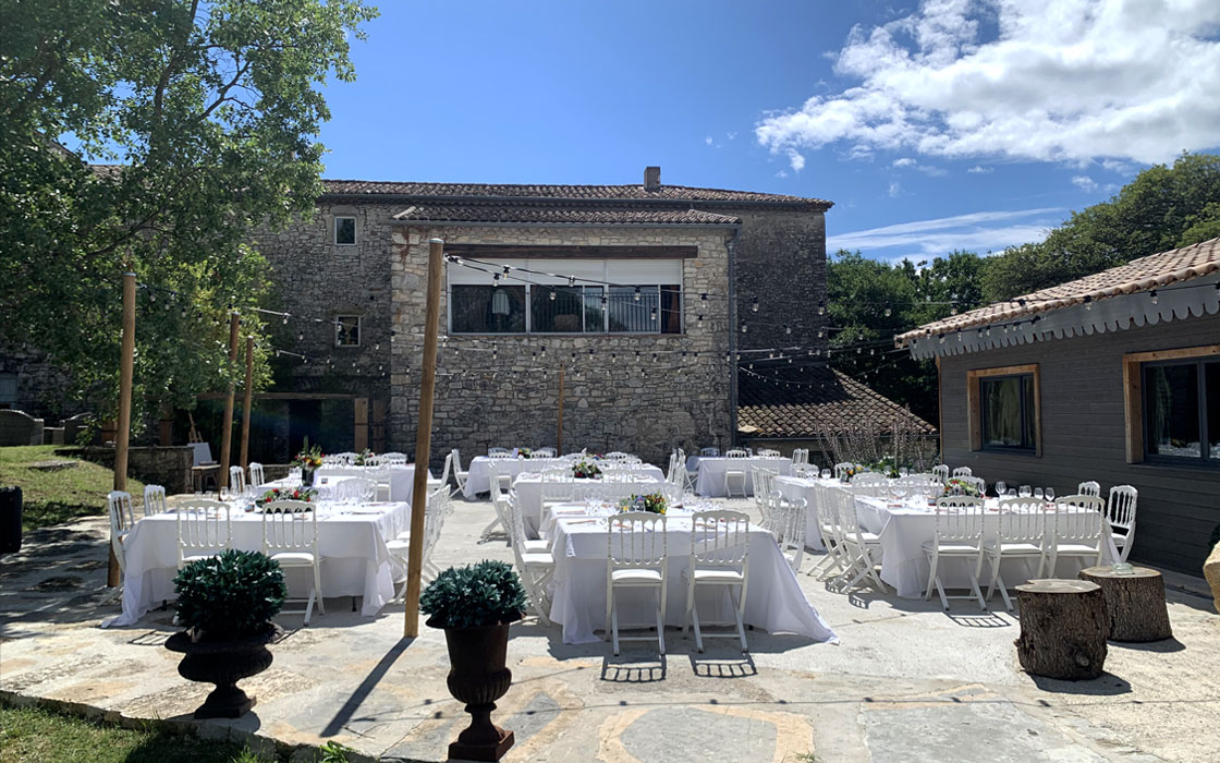Terrasse avec table blanches et maison en pierre au fond pour lancement ed produitt en provence